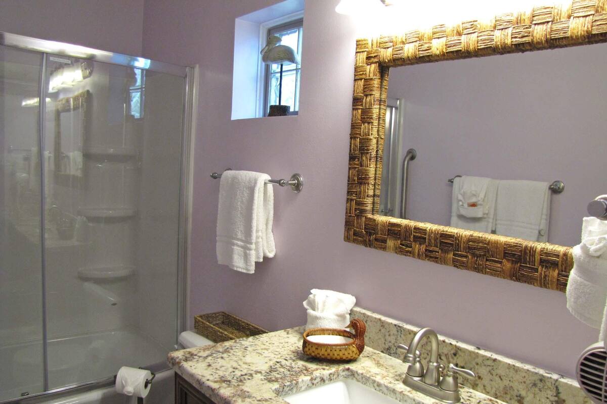 A bathroom with a shower, a sink, a mirror, and a window.