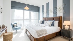 A modern bedroom with a large bed, a desk, a chair, and a window with a view of the city. - Maison Privee - Exclusive Apt w/ Burj Khalifa Next Door (Dubai)