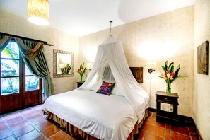 A bedroom with a four-poster bed, a nightstand with a lamp, and a window with curtains. - Casa San Juan (Antigua Guatemala)