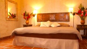 A hotel room with a large bed, two bedside tables with lamps, a wooden headboard, and a tiled floor.