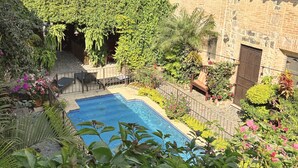 Une piscine entourée d’une végétation luxuriante et un bâtiment en briques avec une porte portant l’inscription « Service aux clients ».