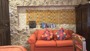 Een gezellige kamer met een stenen muur, een houten kast, een rode bank met kleurrijke kussens en een boekenkast vol boeken.