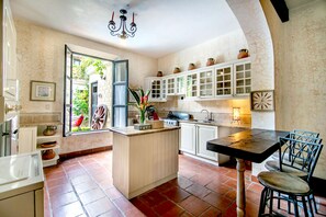 Une cuisine dotée d’un îlot central, de meubles blancs et offrant une vue sur l’extérieur grâce à une porte ouverte.