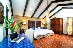 A bedroom with a bed, a desk with a laptop, a wardrobe, and a brick floor.