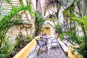 Un petit espace extérieur aménagé avec une terrasse en pierre, entouré d’une végétation luxuriante et agrémenté d’un mur décoratif.