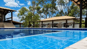 A clear blue swimming pool with tiled edges, surrounded by a covered seating area and a building with a tiled roof. -  Paz e Tranquilidade - Casa para 20 pessoas com 7 quarto (Capitólio)