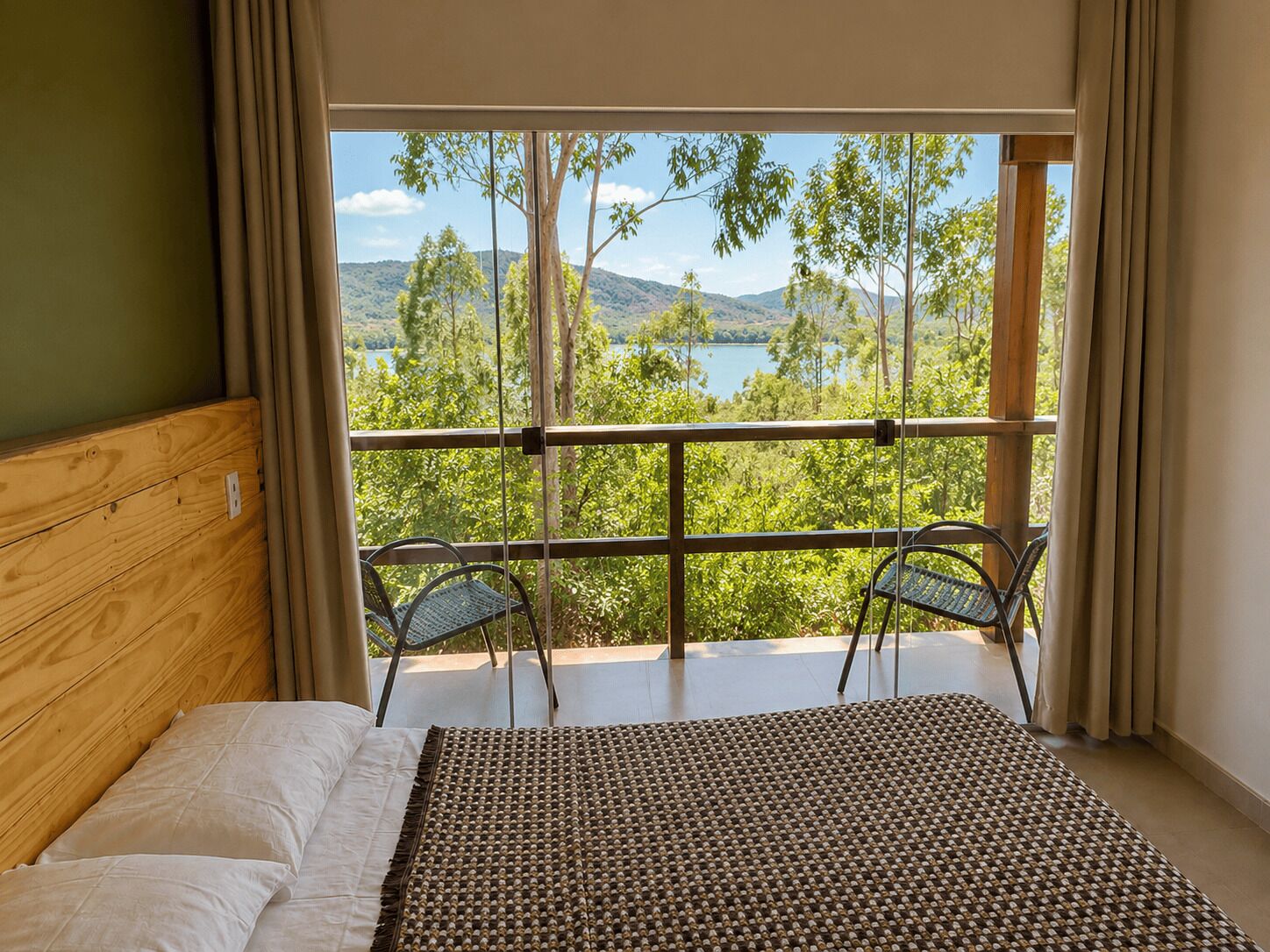A bedroom with a large window, a bed, and two chairs.