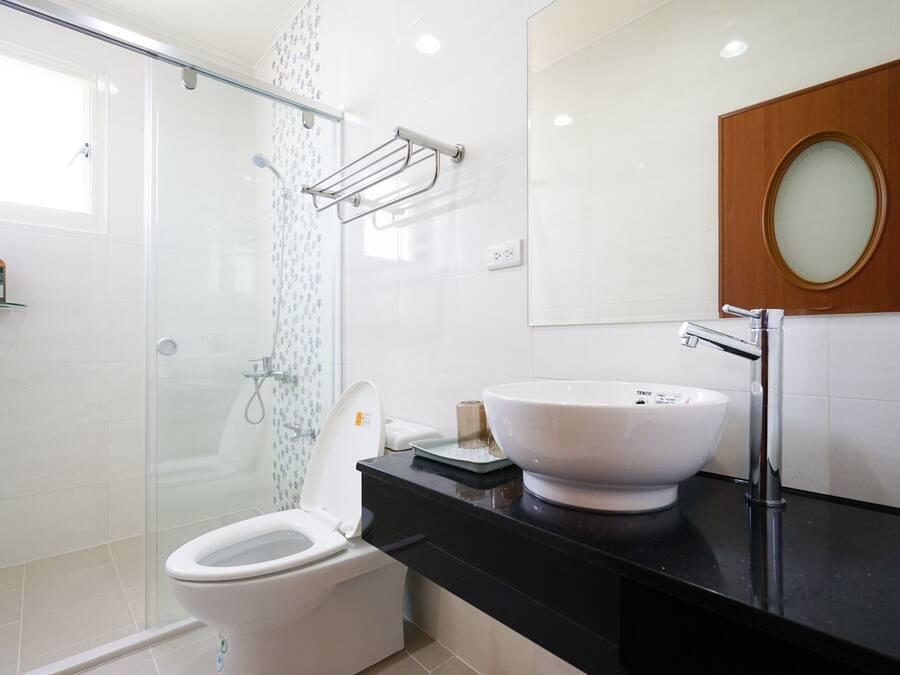 A modern bathroom with a glass shower enclosure, a white toilet, a black countertop, a white sink, and a wooden medicine cabinet.