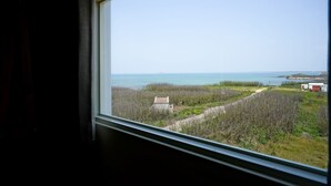 Vista da janela sobre a costa, com um caminho que leva a um edifício, um corpo de água e uma ilha ao longe.