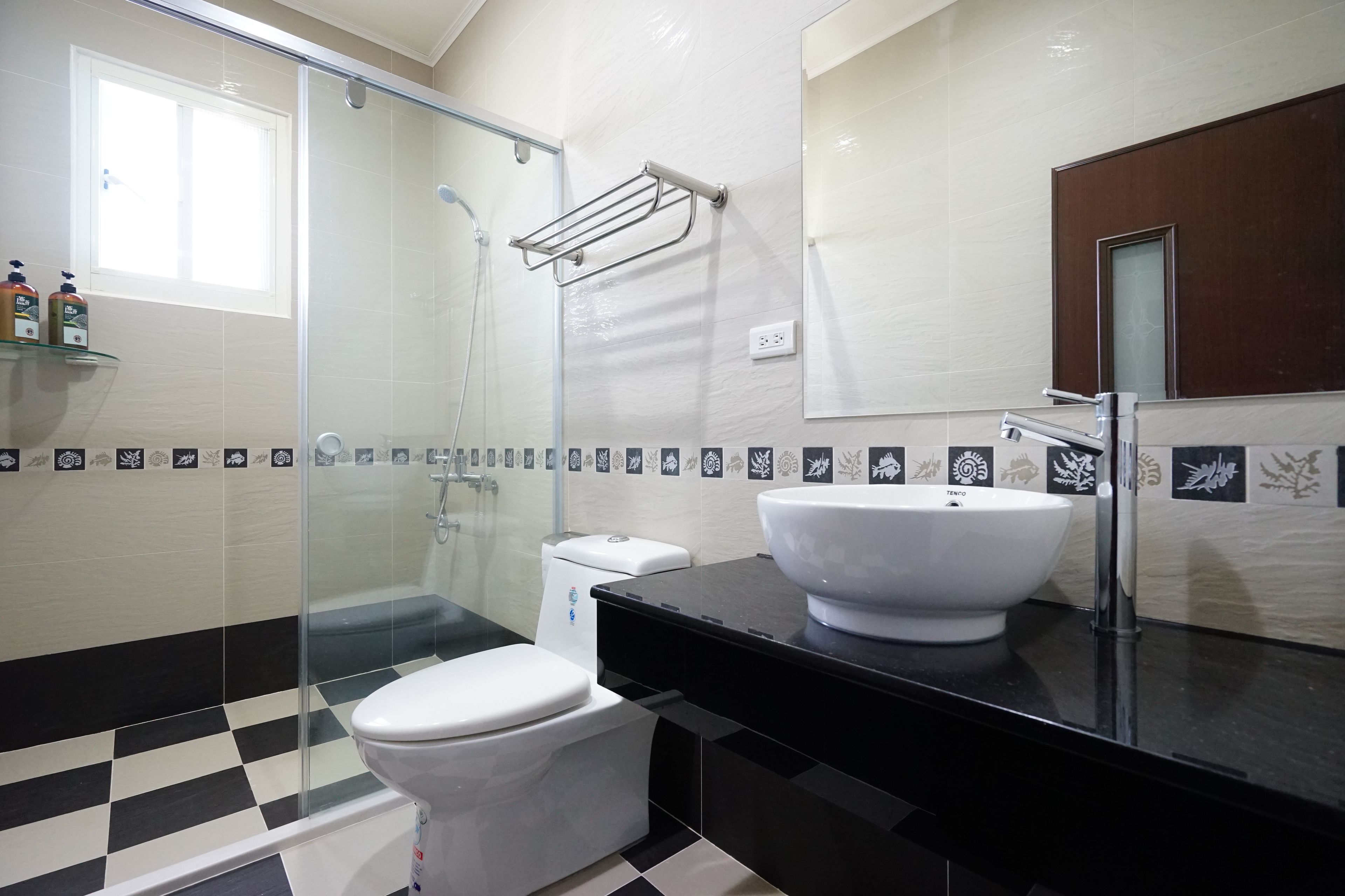 A modern bathroom with a glass shower enclosure, a white toilet, and a black countertop with a white sink.