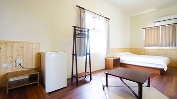 A hotel room with a bed, a desk, a small table, a wardrobe, and a window with curtains.