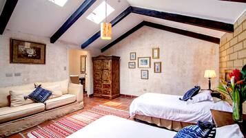 A room with a high ceiling, exposed beams, a sofa, two beds, a wooden wardrobe, and a wall with framed pictures.