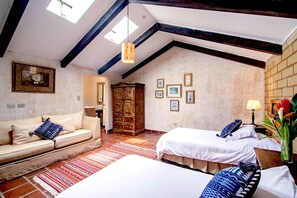 Een kamer met een hoge plafond, zichtbare balken, een bank, twee bedden, een houten garderobe en een muur met ingelijste foto's.