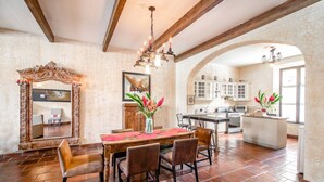 A dining area with a wooden table, chairs, and a mirror. There is a kitchen in the background with cabinets and a countertop. - Casa Santa Catarina (Antigua Guatemala)