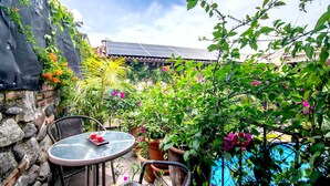 Une terrasse avec une table ronde et des chaises, entourée de plantes en pot et d’une piscine.