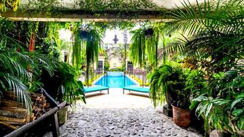 A stone pathway leading to a blue pool surrounded by lush greenery and potted plants.