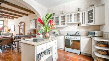 A kitchen with white cabinets, a stove, and a microwave. There is a dining area with chairs and a table.