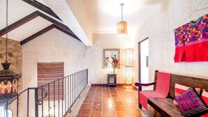 A spacious room with a wooden bench, a hanging tapestry, and a stone wall. - Casa Santa Catarina (Antigua Guatemala)