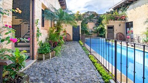 A courtyard with a stone pathway leading to a pool, surrounded by plants and a rustic building with a door and windows. - Casa Santa Catarina (Antigua Guatemala)