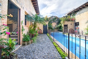 A courtyard with a stone pathway leading to a pool, surrounded by plants and a rustic building with a door and windows. - Casa Santa Catarina (Antigua Guatemala)