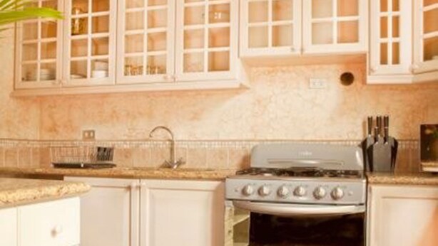 A kitchen with white cabinets, a stove, and a tiled floor. - Casa Santa Catarina (Antigua Guatemala)