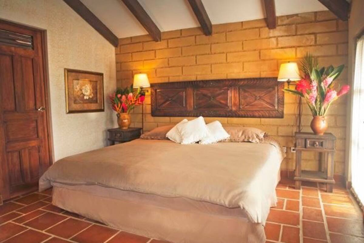 Un dormitorio con una cama grande, cabecera de madera, dos mesitas de noche con lámparas y una pared de ladrillo.