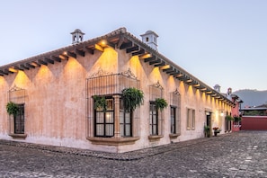 Um edifício histórico com rua de paralelepípedos, janelas grandes com grades de ferro forjado e uma torre de sino.