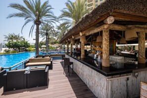 A poolside bar area with wooden deck seating and a pool in the background.