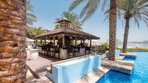 A poolside bar area with a thatched roof, seating, and a view of the pool. - Maison Privee - Beach Access Apt w/ Burj & Sea Views on The Palm (Dubai)