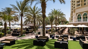 An outdoor lounge area with palm trees, outdoor seating, and umbrellas. - Maison Privee - Beach Access Apt w/ Burj & Sea Views on The Palm (Dubai)