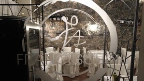 Un restaurante con mesas redondas, sillas blancas y un fondo de pared de piedra.