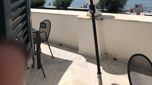 Una terraza con una sombrilla grande, una silla y vistas al mar y un paisaje urbano distante.