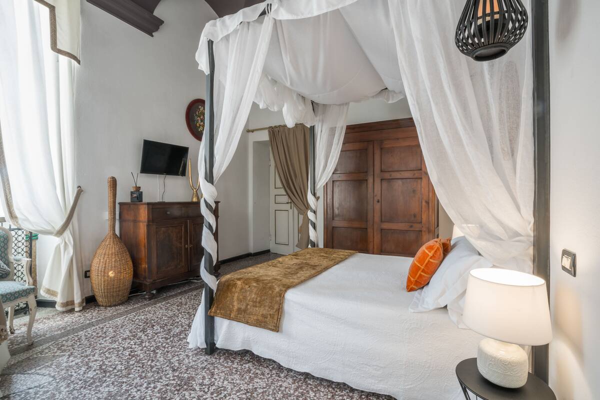 Un dormitorio con una cama con dosel, un televisor en la pared y un florero de mimbre sobre un tocador.