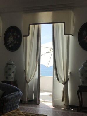 A room with a view of the sea through a door with curtains, a chair, and two vases on the wall. - Villa Shelley Boutique Hotel (Lerici)