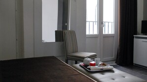 Een hotelkamer met een bed, een stoel, een klein tafeltje met een dienblad met ontbijtartikelen, en een raam met gordijnen.