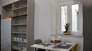 Een compacte keuken met een eethoek, inclusief een tafel met stoelen, een raam met uitzicht en een inbouwplank met servies en glazen.