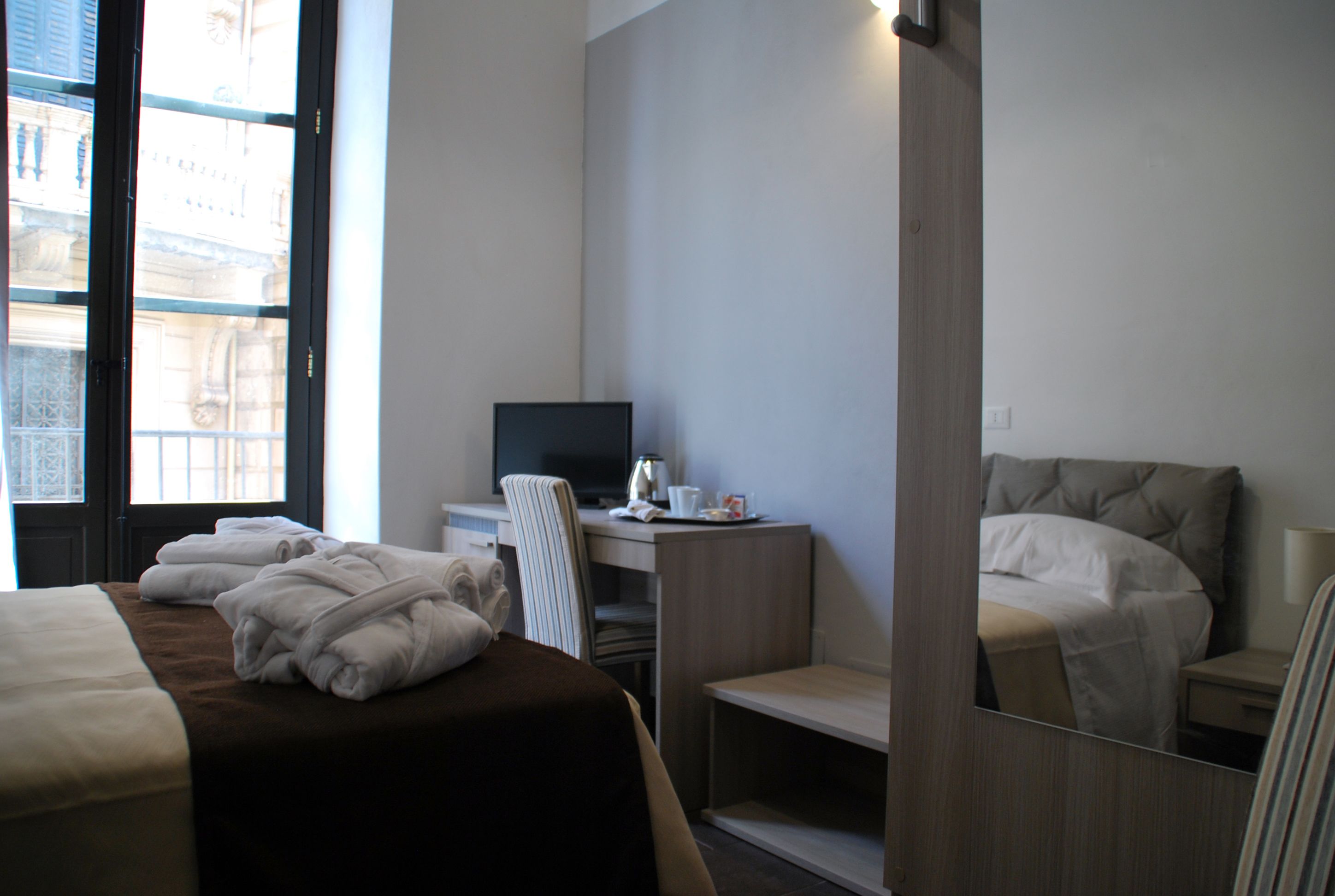 Quarto de hotel com uma cama, uma escrivaninha com computador e um espelho.