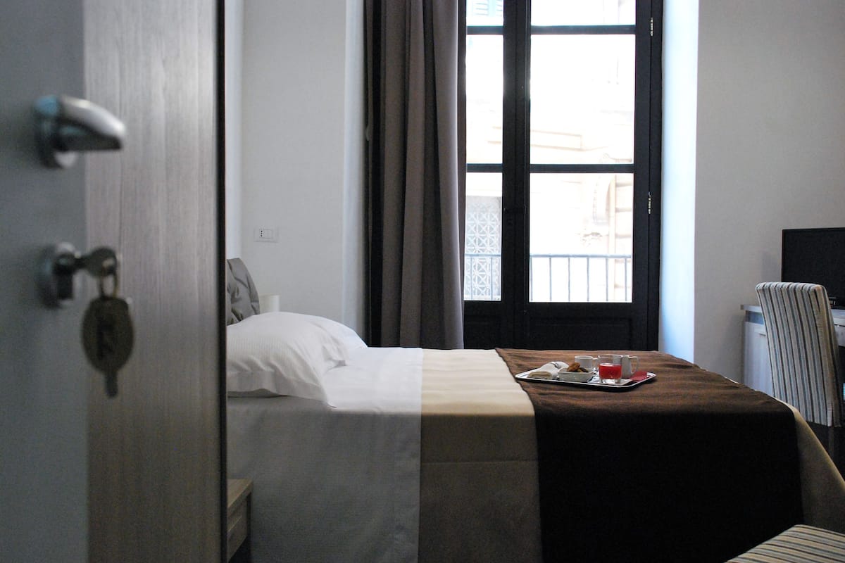 Une chambre d’hôtel avec un lit, un plateau contenant des articles pour le petit-déjeuner, une chaise et une fenêtre avec des rideaux.