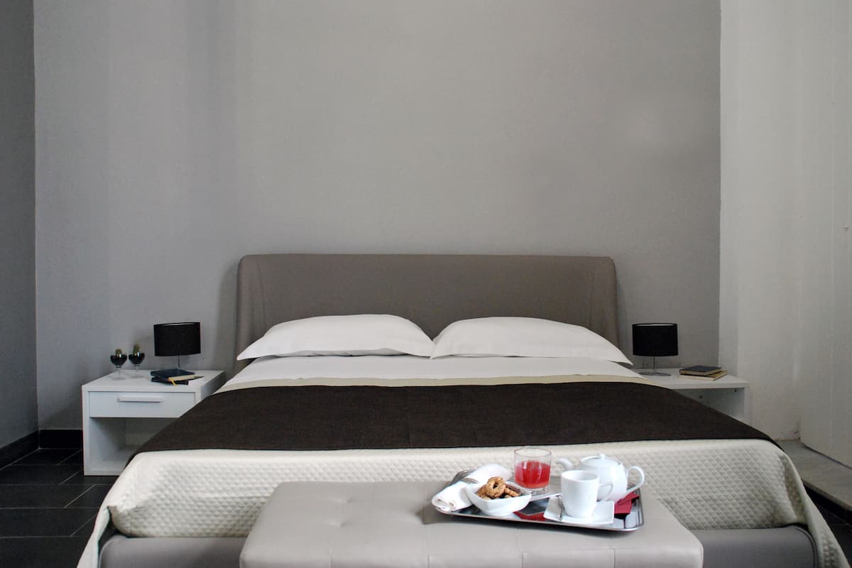 Une chambre d’hôtel moderne avec un lit soigneusement fait, une table de chevet avec une lampe et un plateau contenant des articles pour le petit-déjeuner.