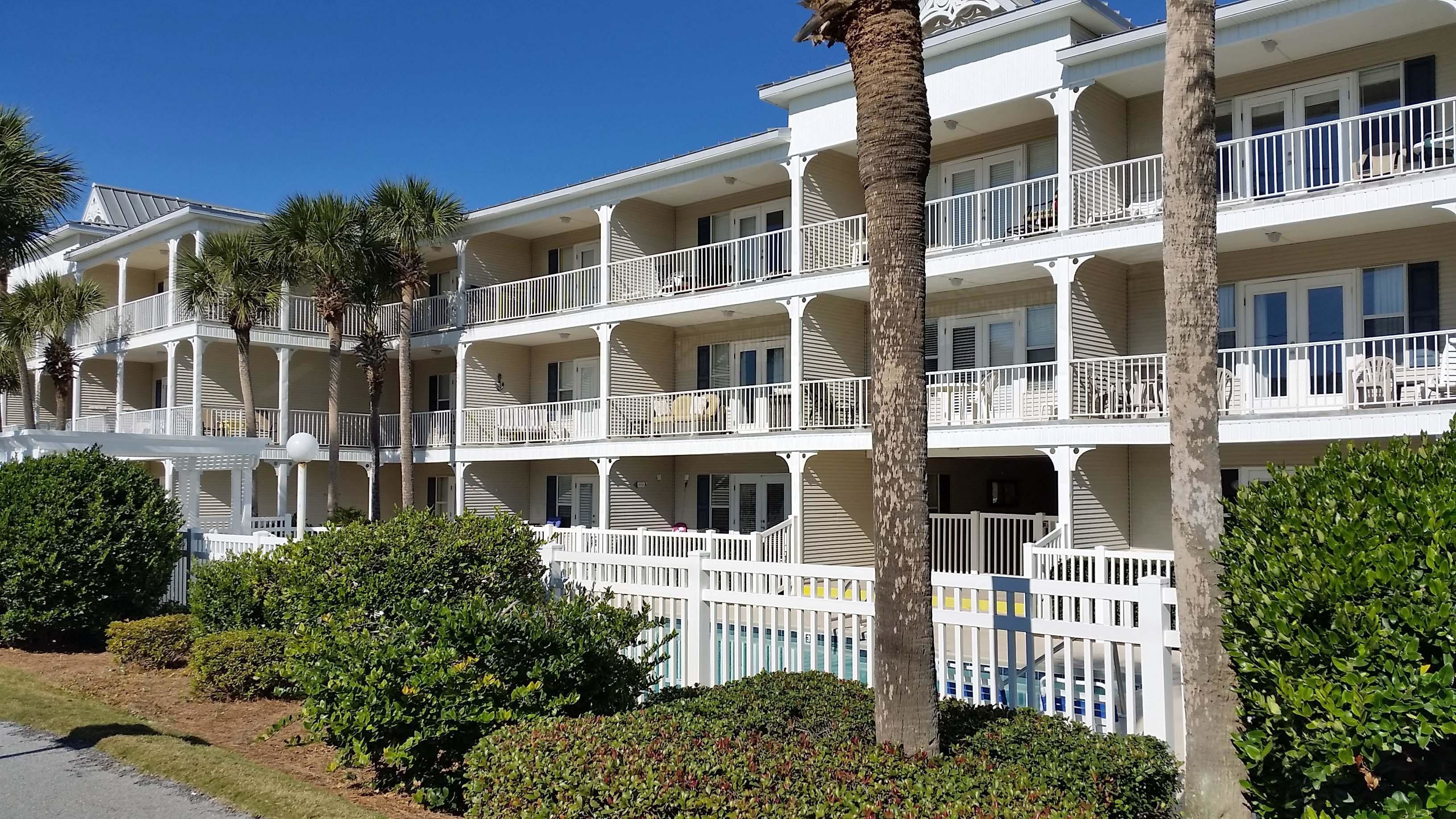 A multi-story hotel with balconies, palm trees, and well-maintained landscaping.