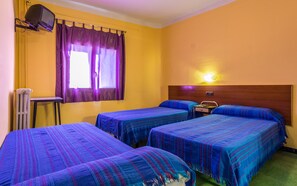 Una habitación de hotel con dos camas individuales, una mesita pequeña, una silla, un televisor montado en la pared y una ventana con cortinas.