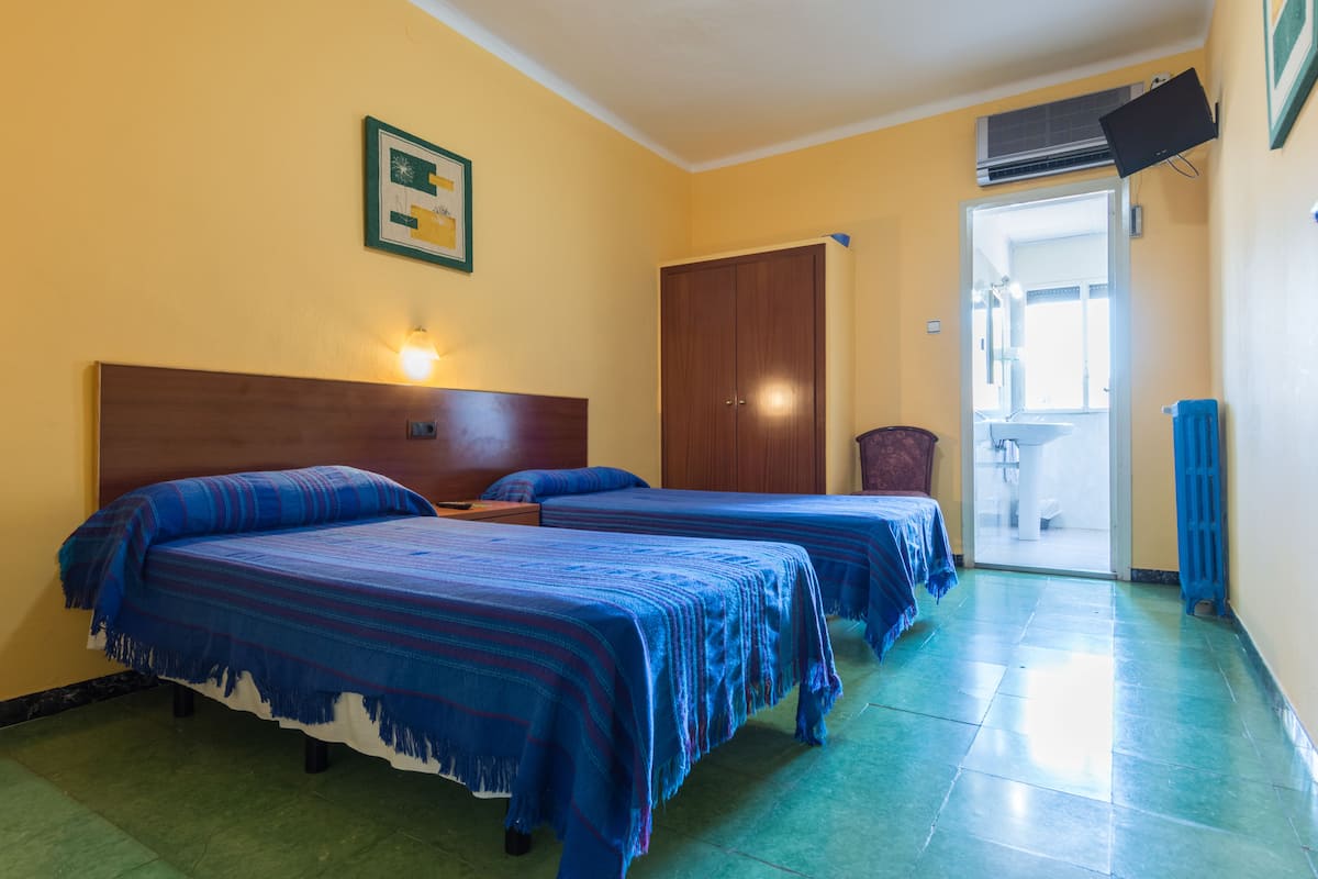 A hotel room with two beds, a wooden headboard, a wall-mounted TV, and a door leading to a bathroom.