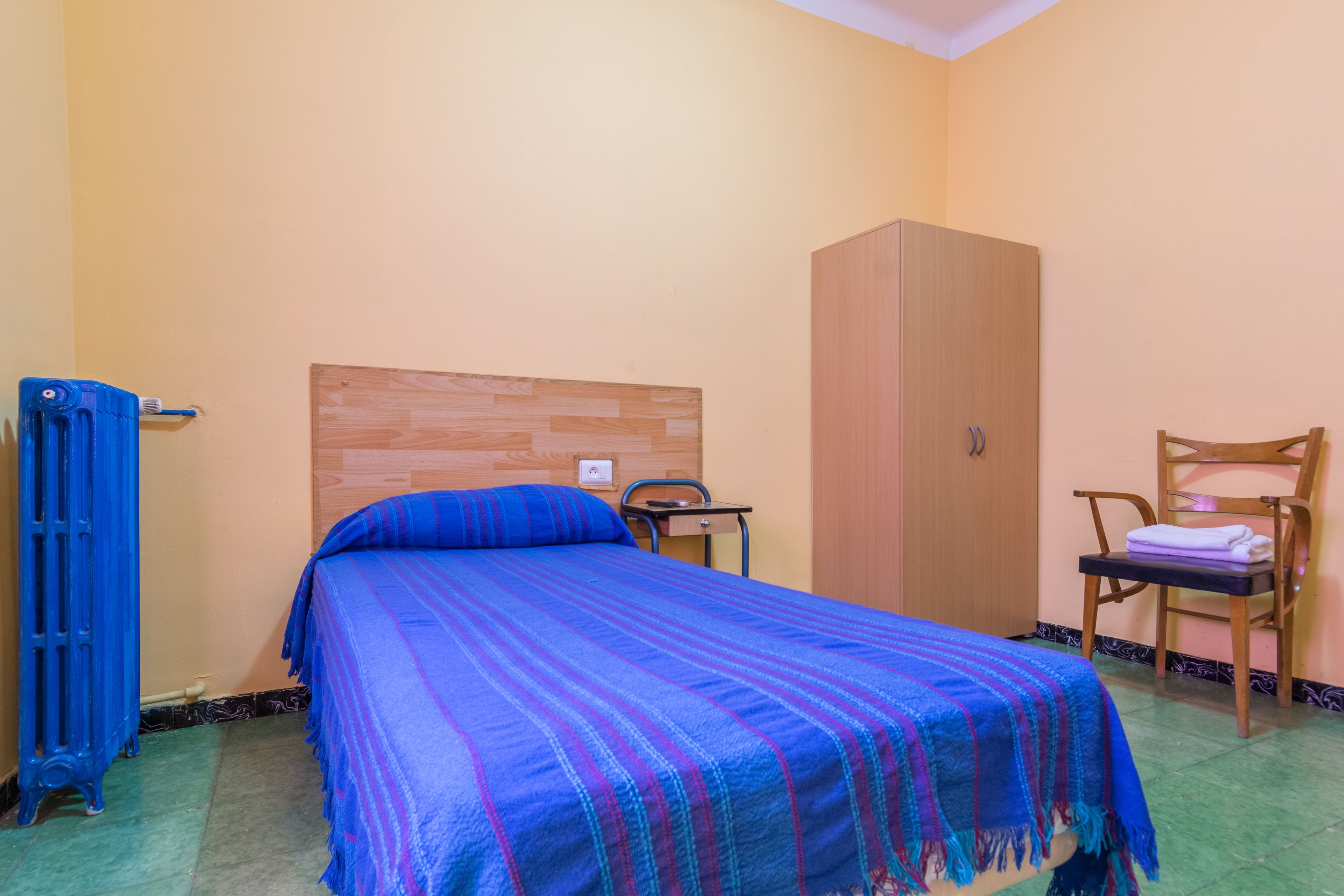 Una habitació amb un llit, un armari de fusta, una cadira i un radiador.
