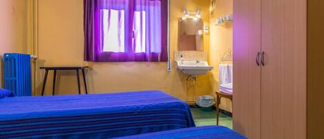 A room with two beds, a window with purple curtains, a sink, and a television mounted on the wall.