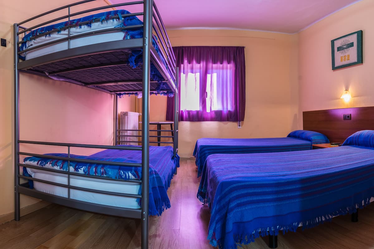 A bunk bed room with two single beds, a wooden headboard, a window with purple curtains, and a wall-mounted light fixture.