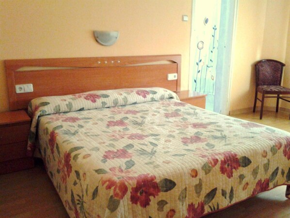 A bedroom with a floral bedspread, wooden headboard, and a chair in the corner. - Hostal Urgell (Balaguer)