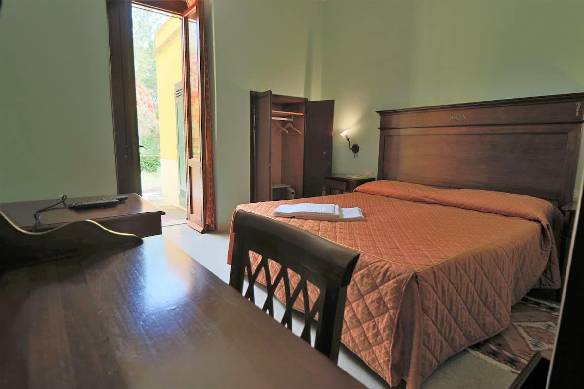 Quarto com cama de madeira, escrivaninha com cadeira, guarda-roupa e mesa de cabeceira.