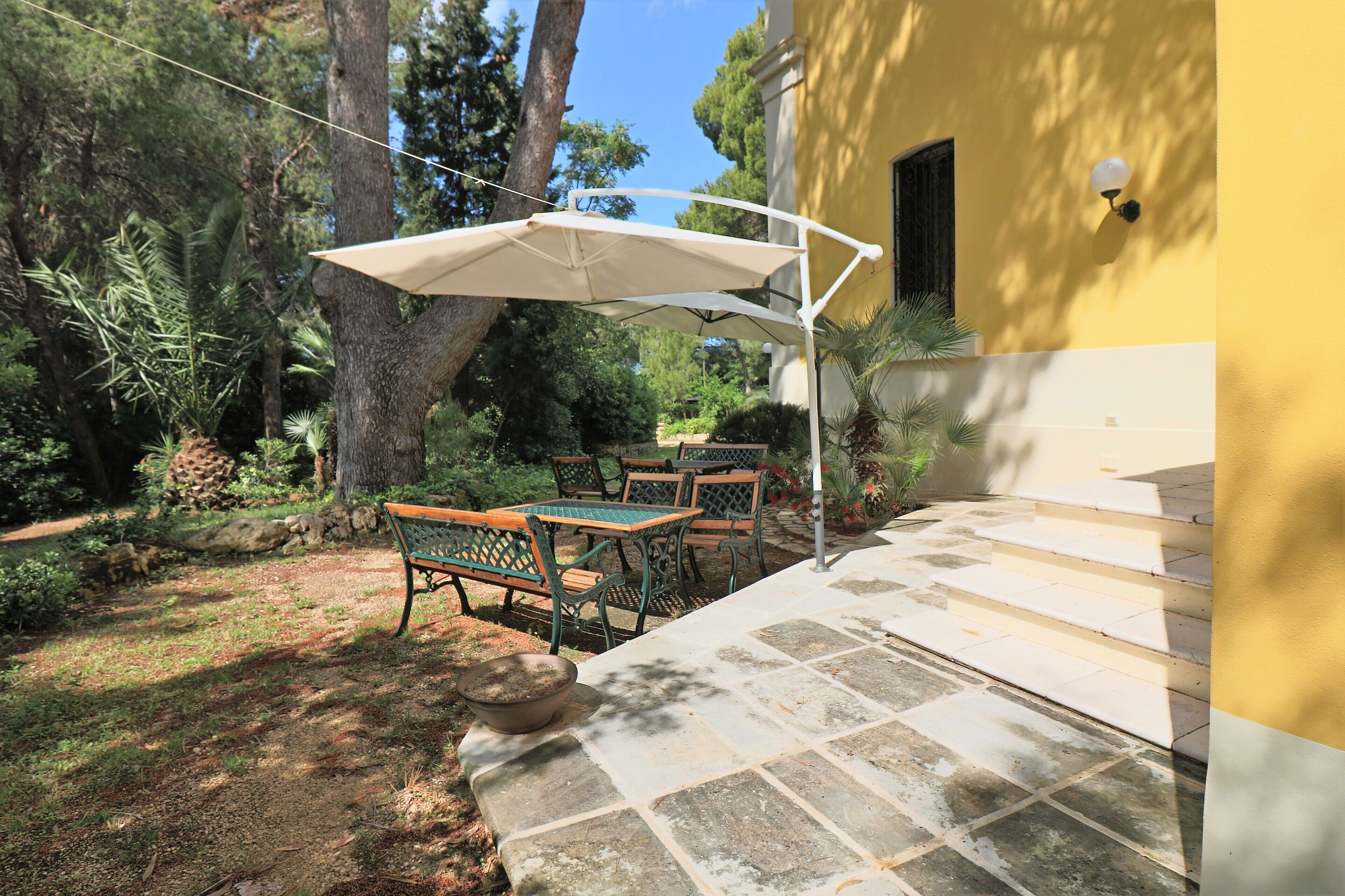 Une terrasse extérieure avec une table et des chaises, un grand parasol et un chemin de pierre menant à un bâtiment.
