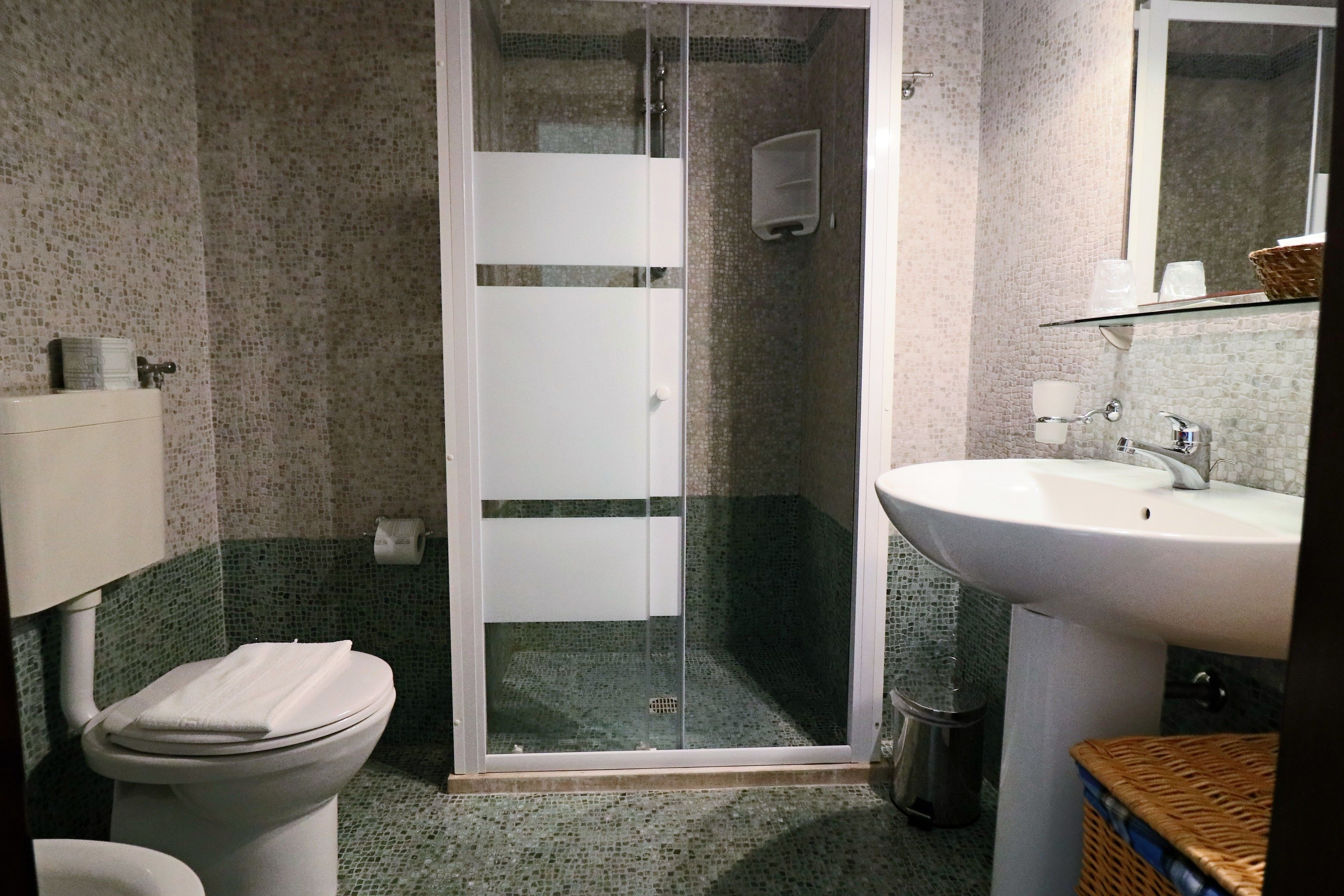 Un baño con inodoro, ducha con mampara de vidrio, lavamanos y espejo.