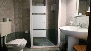 Un baño con inodoro, ducha con mampara de vidrio, lavamanos y espejo.